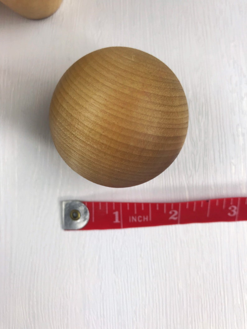 May include: A close-up of a light brown wooden ball, approximately 1 inch in diameter, with a smooth, slightly textured surface. The ball is sitting on a white surface.