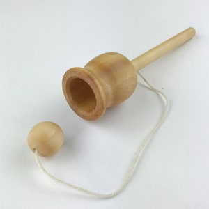 May include: A wooden toy with a string and a ball. The toy is shaped like a cup with a long handle. The ball is attached to the string and can be swung into the cup.