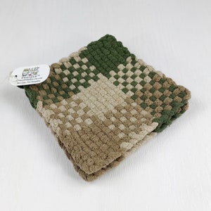 May include: A green and brown woven kitchen dishcloth or pot holder. The dishcloth is folded in half and has a tag attached that reads "Magic Designs" and includes a website address and location.