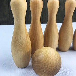 May include: A set of wooden bowling pins and a ball, all in a natural wood color. The pins are arranged in a row, and the ball is in front of them.