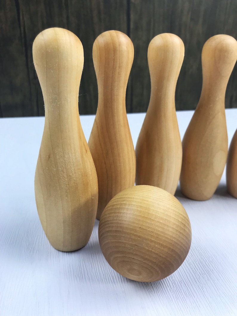 May include: A set of wooden bowling pins and a ball, all in a natural wood color. The pins are arranged in a row, and the ball is in front of them.