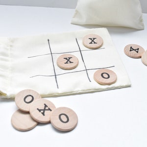 May include: A white fabric bag with a black tic-tac-toe board printed on it. The bag contains wooden game pieces with the letters X and O printed on them.
