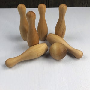 May include: A set of wooden bowling pins and a ball. The pins are light brown and the ball is a slightly darker shade of brown. The set is arranged on a white surface.