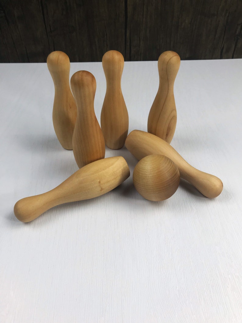 May include: A set of wooden bowling pins and a ball. The pins are light brown and the ball is a slightly darker shade of brown. The set is arranged on a white surface.