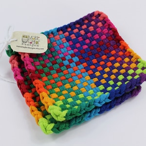 May include: Two square, woven washcloths in a rainbow of colors, including red, orange, yellow, green, blue, and purple. The washcloths are stacked, with a tag attached that reads "Maisie Taylor Designs".