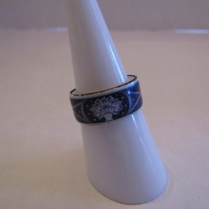 Puede incluir: Un anillo de cerámica azul y blanco con un diseño floral. El anillo está en un soporte de anillo blanco.