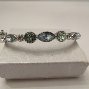 Puede incluir: Un brazalete de plata con una fila de piedras facetadas de color azul claro y verde.