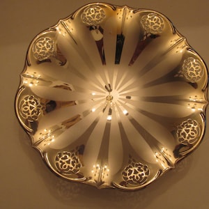 May include: A silver serving bowl with a scalloped edge and a decorative design. The bowl has a shiny, reflective surface and a radial pattern.