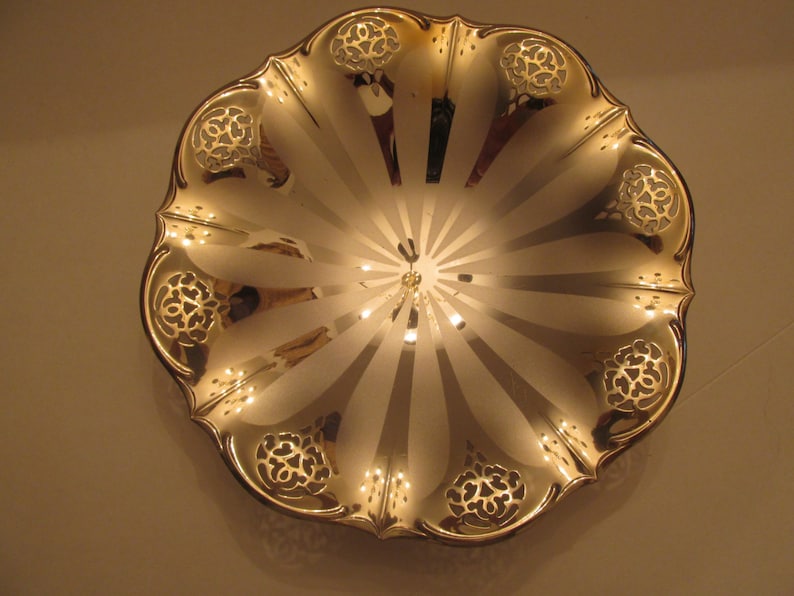May include: A silver serving bowl with a scalloped edge and a decorative design. The bowl has a shiny, reflective surface and a radial pattern.