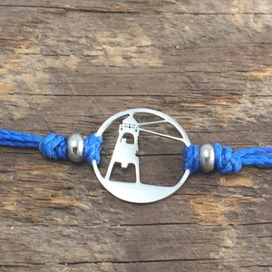 May include: A silver bracelet with a lighthouse charm and blue cord. The charm is a circle with a cut-out design of a lighthouse.
