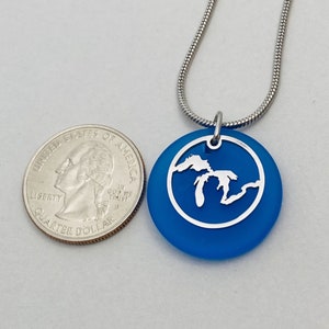 May include: A silver necklace with a blue glass pendant featuring a cutout of the Great Lakes. The pendant is about the size of a 25 pence coin.