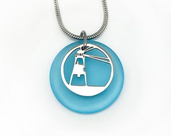 May include: A silver lighthouse pendant necklace with a light blue glass circle. The lighthouse is cut out of the silver and the glass is behind it.