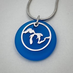 May include: A blue glass pendant necklace with a silver chain and a cutout of the Great Lakes.