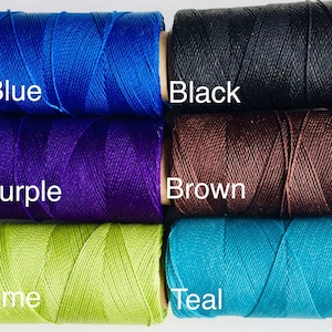 Op de afbeelding: Vijf spoelen garen in verschillende kleuren: blauw, paars, bruin, limoengroen en teal. De spoelen zijn gelabeld met de kleurennamen.