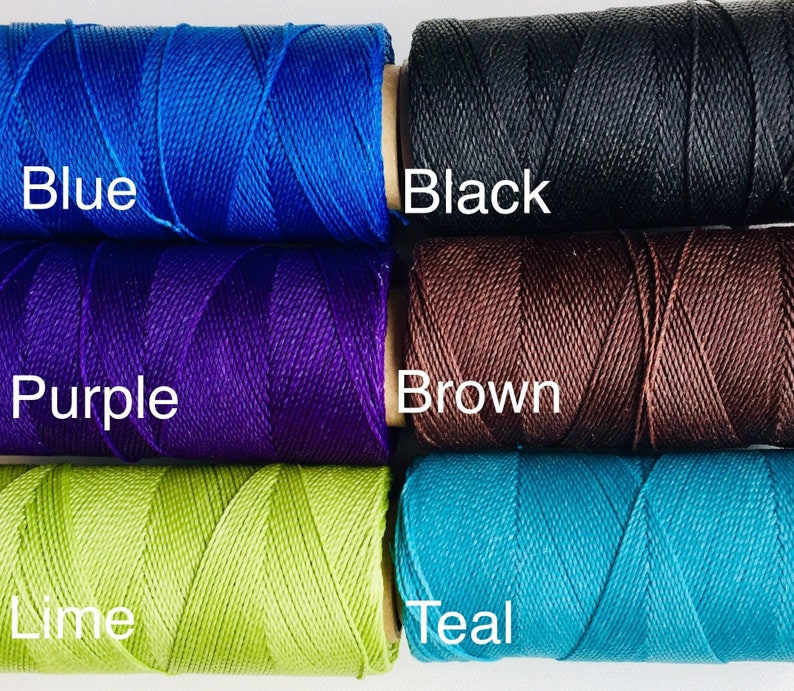 Op de afbeelding: Vijf spoelen garen in verschillende kleuren: blauw, paars, bruin, limoengroen en teal. De spoelen zijn gelabeld met de kleurennamen.