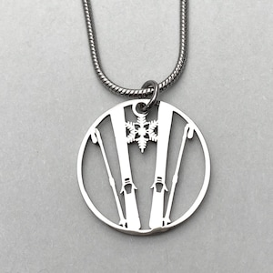 May include: A silver necklace with a circular pendant featuring a cutout design of two pairs of skis and ski poles with a snowflake in the center.
