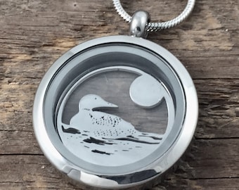 May include: A silver locket necklace with a clear glass insert featuring a loon silhouette on a lake with a moon in the background.