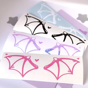 May include: Four sheets of vinyl stickers with different colored bat wings. The wings are outlined in black and have a gradient of pink, purple, and blue. The stickers are perfect for adding a touch of whimsy to laptops, water bottles, or journals.
