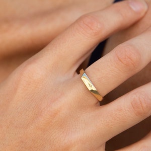 Op de afbeelding: Een gouden ring met een licht hellende, platte bovenkant.