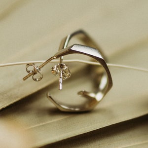 Op de afbeelding: Een zilveren geometrische oorbel met een uniek ontwerp. De oorbel ligt op een beige achtergrond.