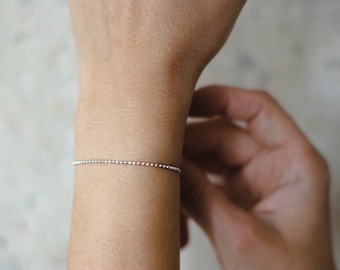 May include: A silver beaded bracelet on a person's wrist.