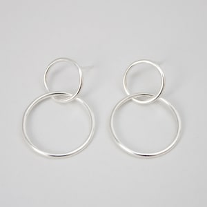 May include: A pair of silver earrings with two interlocking circles. The larger circle is about 1 inch in diameter and the smaller circle is about 1/2 inch in diameter.