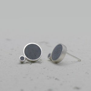 May include: A pair of silver stud earrings with a dark grey circular design. The larger circle has a smaller circle attached to it.