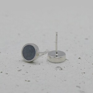 May include: A pair of silver stud earrings with a round, dark gray concrete inlay.