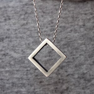 May include: A silver chain necklace with a square pendant. The pendant is hollow and has a geometric design.