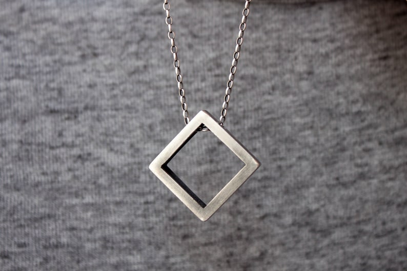 May include: A silver chain necklace with a square pendant. The pendant is hollow and has a geometric design.