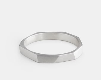 May include: A silver-colored ring with a faceted, geometric design. The ring has a flat, octagonal shape with a brushed metal finish. The ring is a simple, modern piece of jewelry.