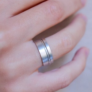Op de afbeelding: Een zilveren ring met twee banden, waarvan er &eacute;&eacute;n iets breder is dan de andere, gedragen aan een vinger.