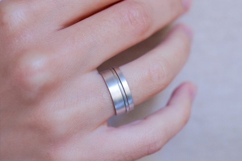 Op de afbeelding: Een zilveren ring met twee banden, waarvan er &eacute;&eacute;n iets breder is dan de andere, gedragen aan een vinger.
