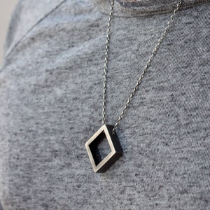 May include: A silver chain necklace with a square pendant. The pendant is made of metal and has a hollow center.