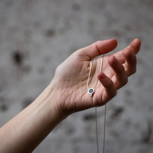 Puede incluir: Un collar de cadena de plata con un peque&ntilde;o colgante redondo con una piedra negra.