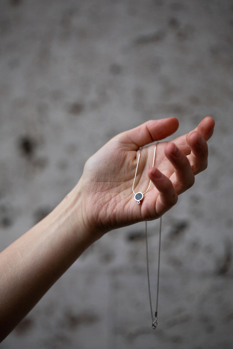 Puede incluir: Un collar de cadena de plata con un peque&ntilde;o colgante redondo con una piedra negra.