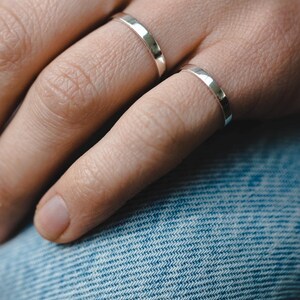 Op de afbeelding: Twee zilveren ringen aan een vinger. De ringen zijn simpel en hebben een gladde, gepolijste afwerking.