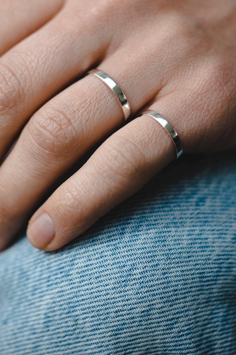 Op de afbeelding: Twee zilveren ringen aan een vinger. De ringen zijn simpel en hebben een gladde, gepolijste afwerking.