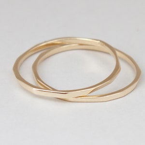 May include: Two gold-toned metal rings, one slightly larger than the other, are stacked on top of each other. The rings are both smooth and have a slightly rounded shape.