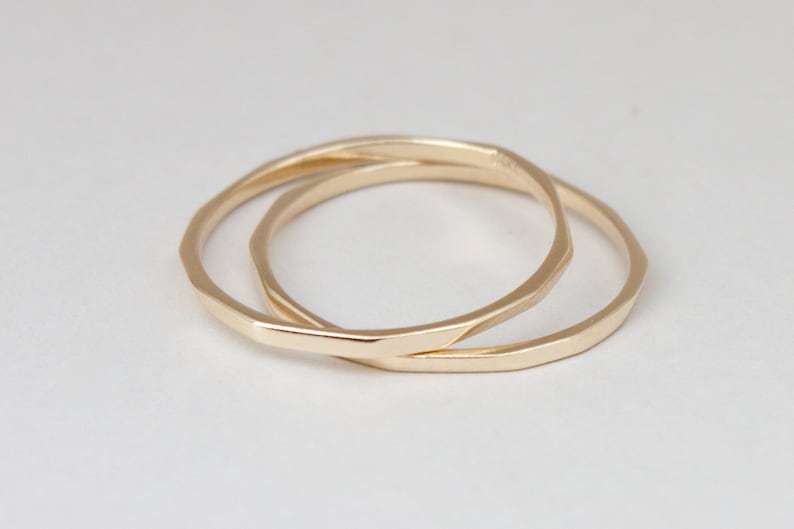 May include: Two gold-toned metal rings, one slightly larger than the other, are stacked on top of each other. The rings are both smooth and have a slightly rounded shape.