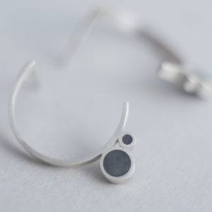 Puede incluir: Un par de pendientes de plata con un dise&ntilde;o curvo y acentos circulares negros.