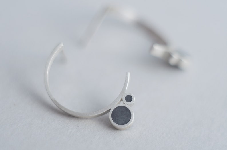 Puede incluir: Un par de pendientes de plata con un dise&ntilde;o curvo y acentos circulares negros.