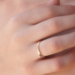 May include: A thin gold band ring worn on the ring finger of a hand.