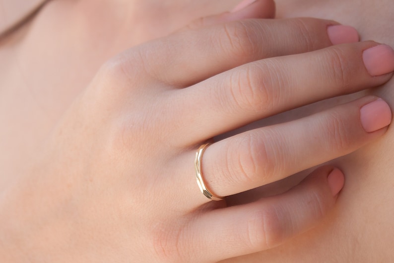 May include: A thin gold band ring worn on the ring finger of a hand.