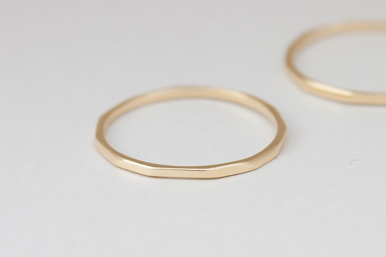 May include: Two gold hammered rings, one is slightly larger than the other. The rings are simple and have a matte finish.