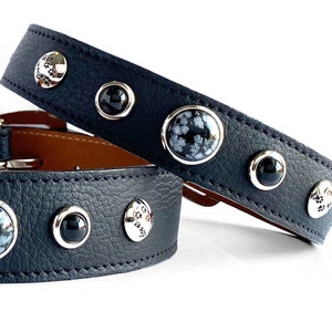 May include: Black leather dog collar with silver accents and decorative stones. The collar has a silver charm with the word "paw" and a paw print.