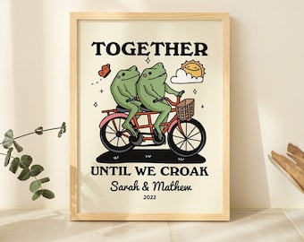 Könnte beinhalten: Ein gerahmter Druck mit einer skurrilen Illustration von zwei Fröschen, die zusammen Fahrrad fahren. Der Text lautet "Together Until We Croak" mit den Namen "Sarah & Matthew" und dem Jahr "2022" darunter.