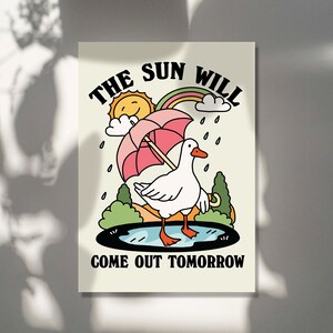 Op de afbeelding: Een witte gans met een roze paraplu loopt door een plas. De tekst "THE SUN WILL COME OUT TOMORROW" staat onder de gans.