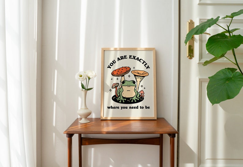May include: A framed print featuring a green frog sitting on a mushroom with the text "You are exactly where you need to be".