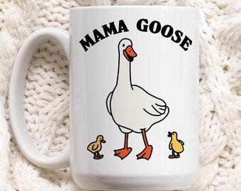 Peut inclure: Une tasse en céramique blanche avec une illustration en noir et blanc d'une oie et de deux oisons. Le texte "Mama Goose" est imprimé en noir sur la tasse.